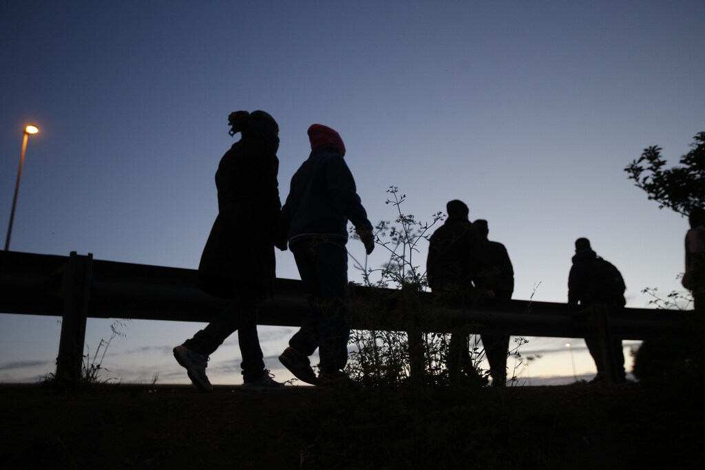 Migrants are seen in silhouette as they walk along the motorway near the Channel Tunnel entrance near Calais, France, August 6, 2015. For most of the 3,000 inhabitants of the "Jungle", a shanty town on the sand dunes of France's north coast, the climax of each day is the nightly bid to sneak into the undersea tunnel they hope will lead to new life in Britain. REUTERS/Peter Nicholls - LR1EB861LHO4Z