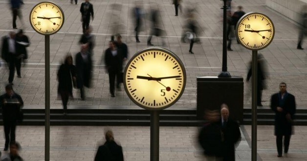 People walk past clocks at Reuters Plaza in London.