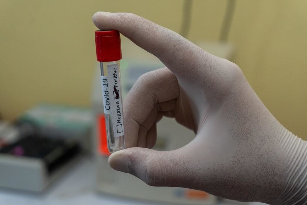 A hand holding an empty blood tube with Positive Coronavirus label.