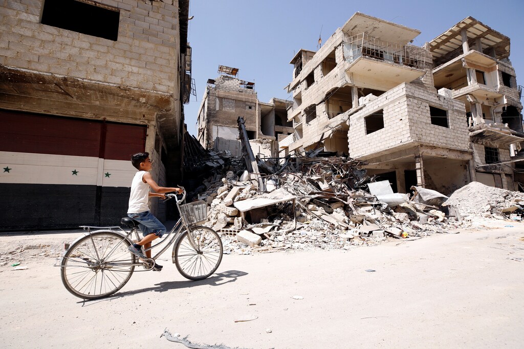 A boy rides on a bicycle along a damaged street in the town of Kafr Batna, in eastern Ghouta, Syria September 5, 2018. REUTERS/Omar Sanadiki - RC1FED85A460