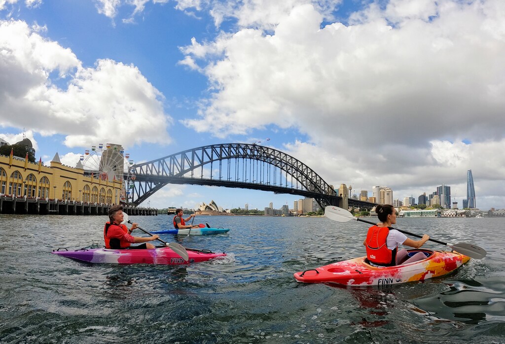 image of kayakers on the 'Clean Up Kayak' tour paddle near the Sydney Harbour Bridge while to helping collect rubbish and plastic from the water in Sydney, Australia.