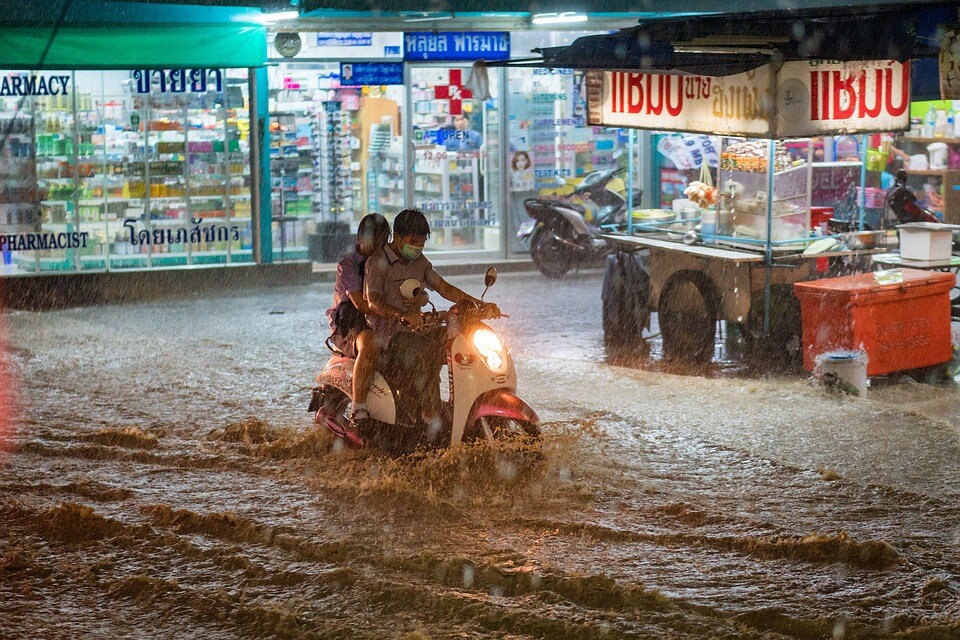 floods people driving scooter through flooded street damages