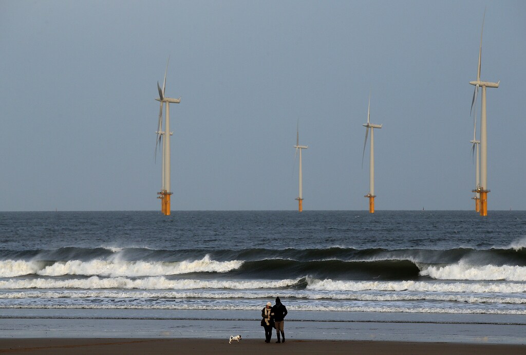 A couple walk their dog on Redcar beach past an offshore wind farm in Redcar, northeast England January 11, 2015. REUTERS/Andrew Yates (BRITAIN - Tags: ENVIRONMENT SOCIETY ENERGY) - LM1EB1B106I01