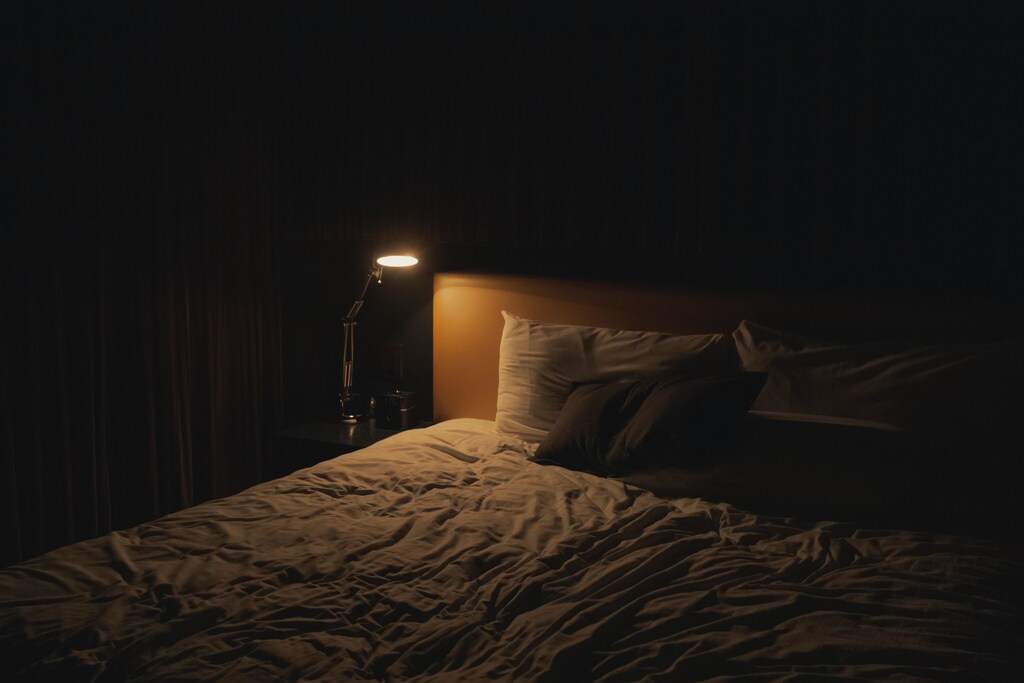 a picture of a bedside table with a lamp on it shining its light over a bed