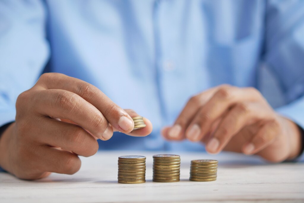 Cost of living crisis: A person counting money with three stacks of coins.