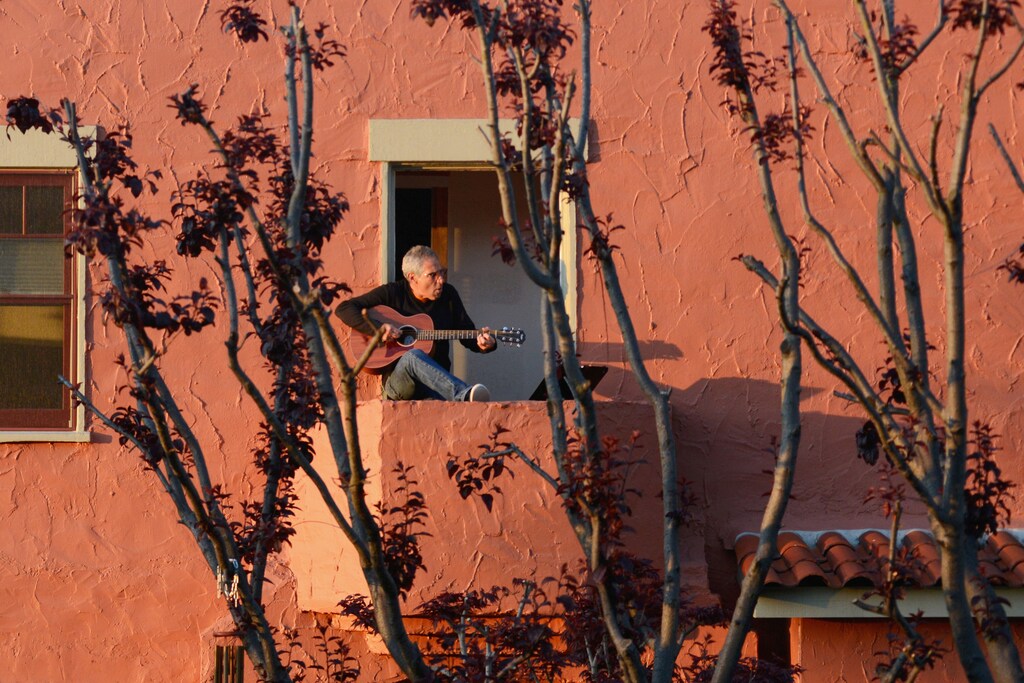 Danny Wertheimer plays guitar and sings to his neighbors from his balcony two days after Californias Governor Gavin Newsom implemented a state wide "stay at home order" directing the states 40 million residents to stay in their homes for the foreseeable future in the face of the fast-spreading coronavirus disease (COVID-19) in Oakland, California, U.S. March 21, 2020. Picture taken March 21, 2020. REUTERS/Kate Munsch TPX IMAGES OF THE DAY - RC2APF9BXFUG