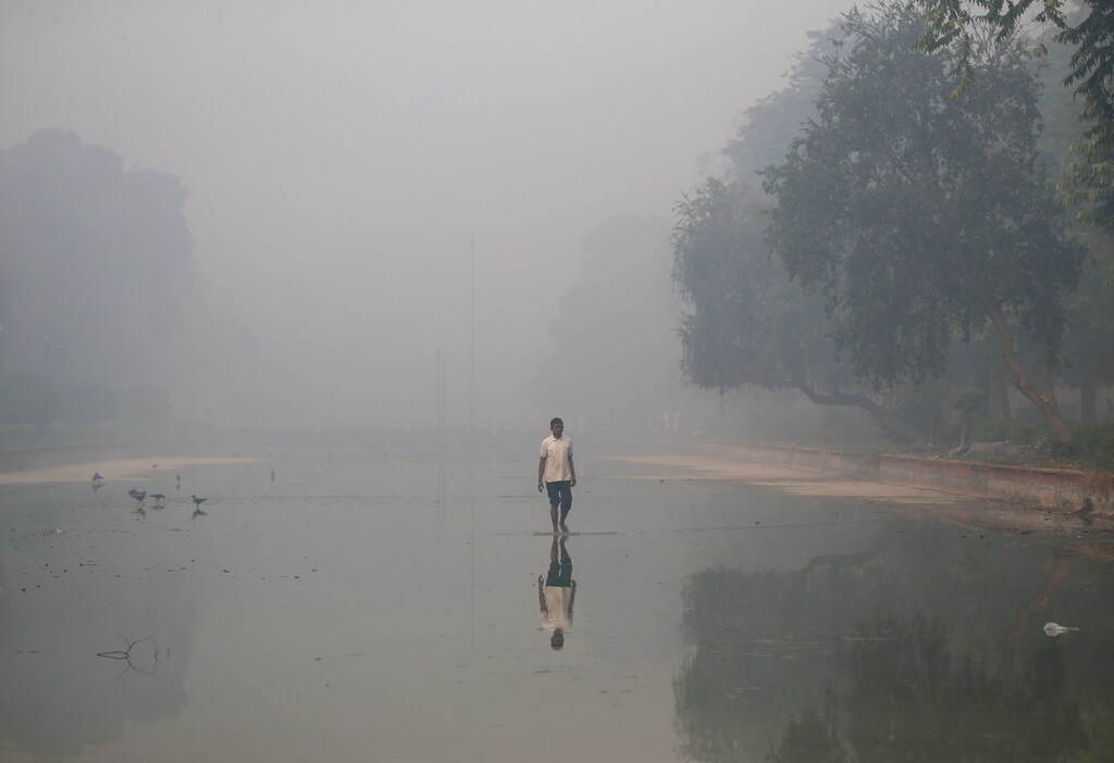 A man walks in a pond on a smoggy morning in New Delhi, India, October 31, 2016