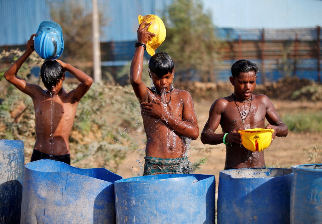 Workers use their helmets to pour water over themselves to cool down on a hot day in India.