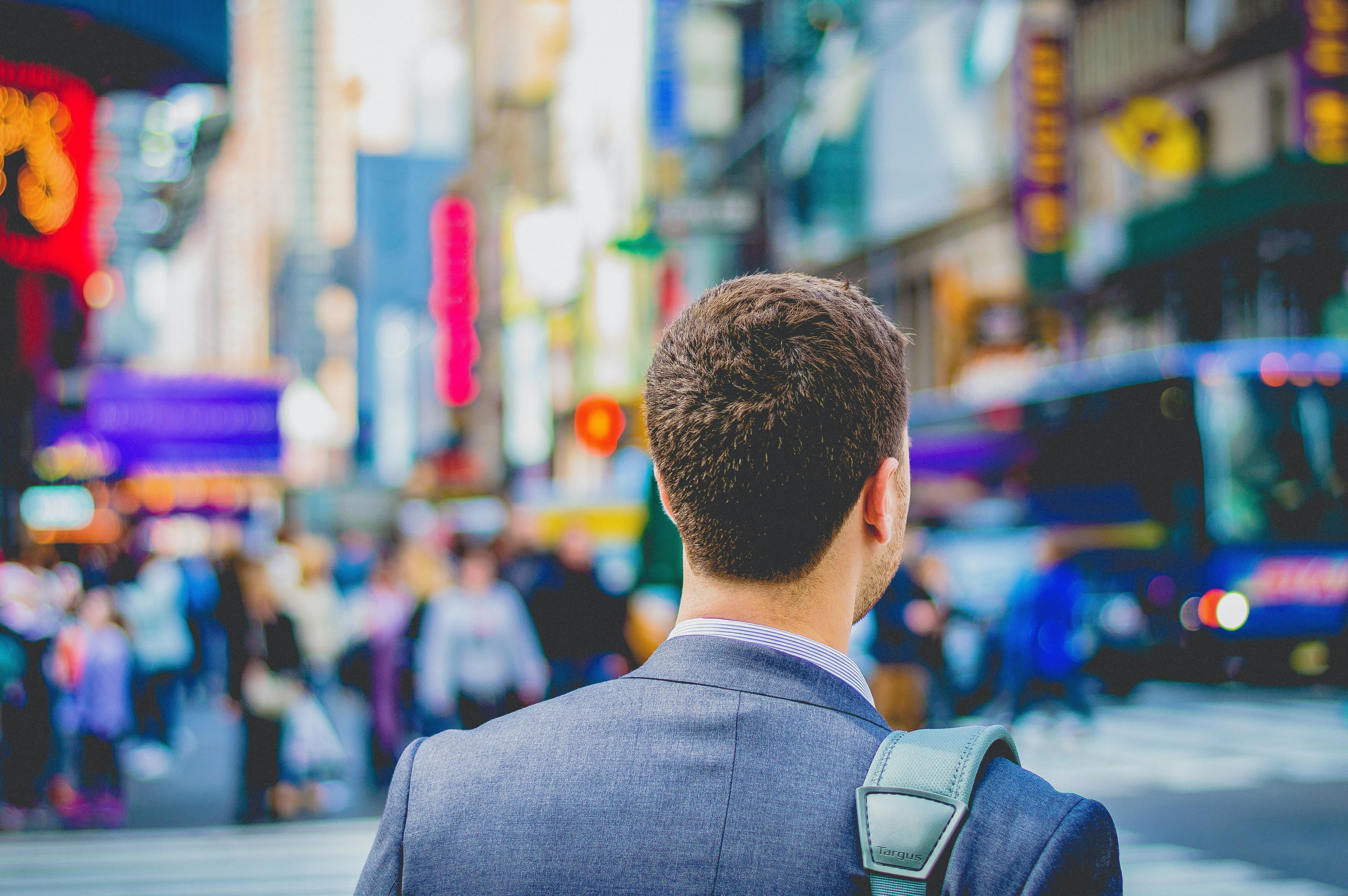 A man wearing a suit facing away from the camera on a busy city road