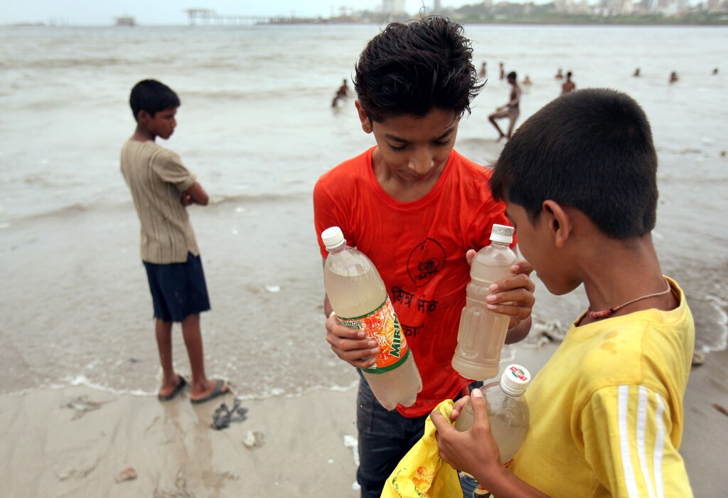 Children hold plastic bottles filled with sea water on a beach in Mumbai August 19, 2006. Thousands of Indians drank from a murky Arabian Sea creek after news spread overnight that its water had miraculously turned sweet and could cure illnesses, police said on Saturday. REUTERS/Punit Paranjpe (INDIA) - RTR1GI1L