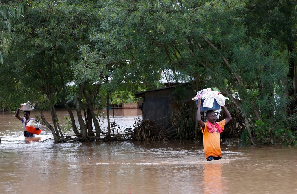 Los residentes llevan sus pertenencias dentro del agua de la inundación mientras evacuan su casa después de que el río Nzoia se desborde y debido al reflujo del lago Victoria, en Nyadorera, condado de Siaya, Kenya, el 2 de mayo de 2020.