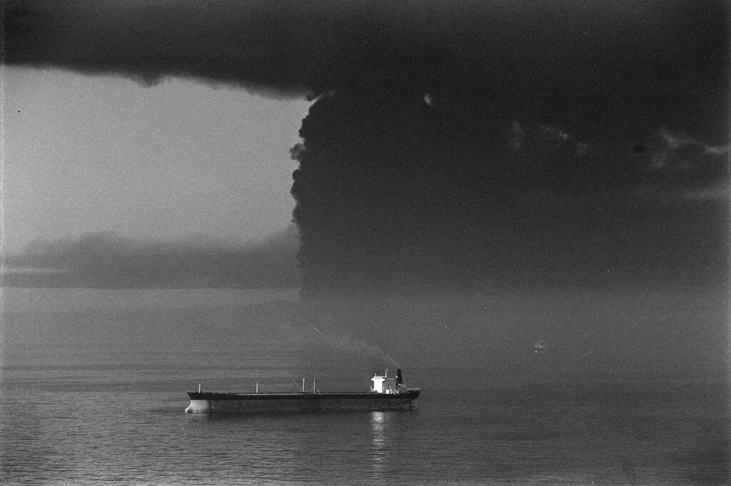 Un petrolero no identificado permanece anclado a cinco millas de la isla de Larak, cerca del estrecho de Ormuz, mientras una enorme columna de humo se eleva tras cuatro petroleros, incluido el Seawise Giant, alcanzados por aviones iraquíes. Esto ocurre en medio de la llamada «Guerra de los Petroleros», cuando los ataques contra la navegación en el Golfo y las operaciones de escolta estadounidenses se intensificaron en el estrecho de Ormuz, en la fase final de la guerra Irán-Irak. 14 de mayo de 1988 REUTERS/Spiros Mantzarlis 88180064