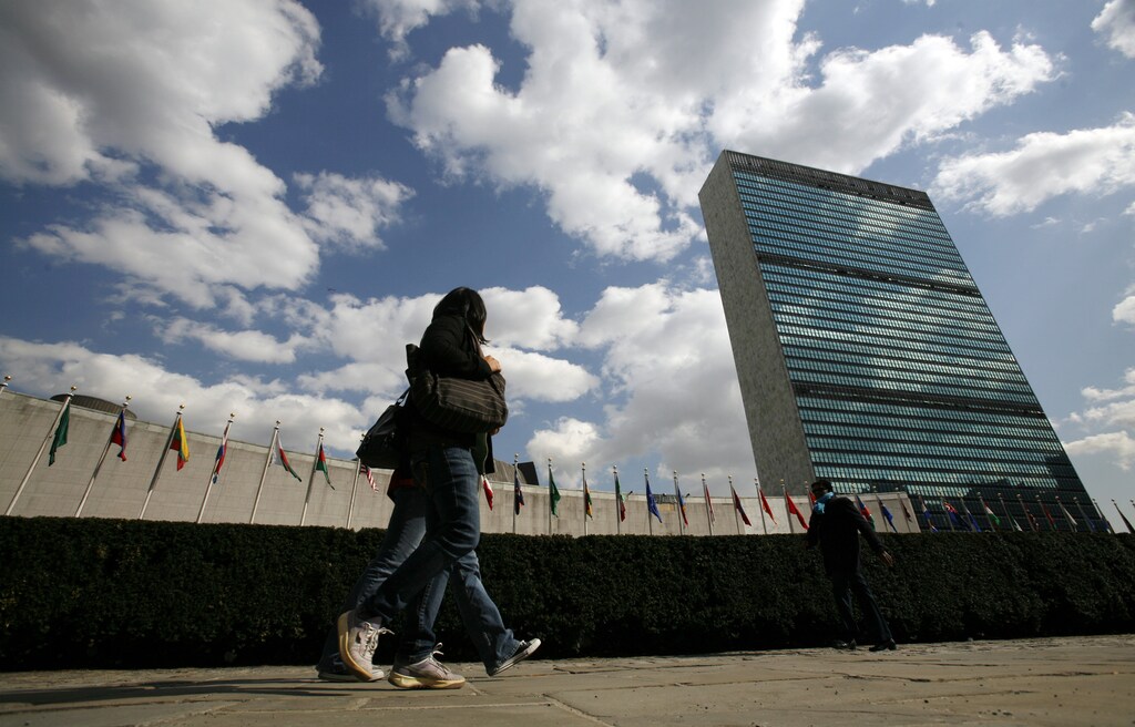 Tourists walk past the United Nations Headquarters in New York. At left is the U.N. General Assembly building and at right is the U.N. Secretariat building