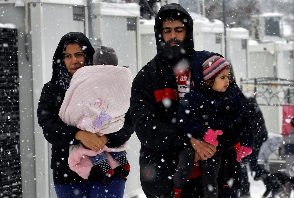 Stranded Syrian refugees carry their children through a show storm at a refugee camp north of Athens, Greece January 10, 2017.REUTERS/Yannis Behrakis - RTX2YCI6