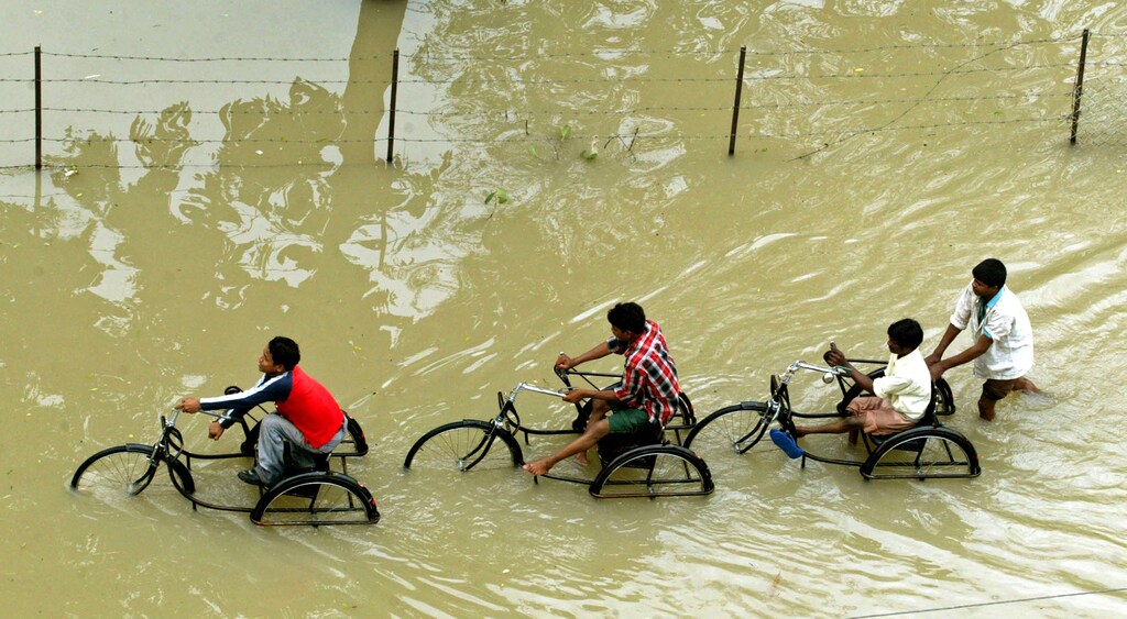 Indian students cycle through a flooded street in Vadodara city, 116 km (72 miles) south of the western Indian city of Ahmedabad July 4, 2005. Indian military helicopters dropped food packets on Monday to thousands of people stranded in vast lakes of water in the west of the country as monsoon rains ebbed after flooding that killed 132 people. REUTERS/Amit Dave VM/KI - RP6DRMUDLDAA