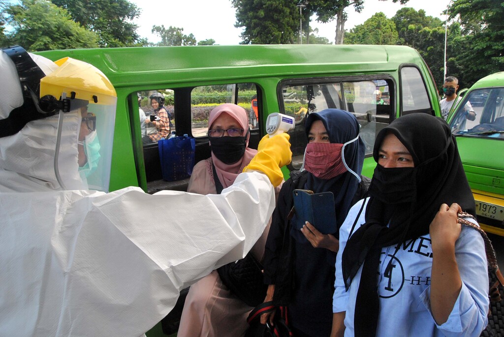 Pasajeros con máscaras faciales tienen la temperatura controlada por un trabajador de la salud en medio de la propagación del brote de la enfermedad coronavirus (COVID-19), en una intersección de la carretera en Bogor, provincia de Java Occidental, Indonesia, el 8 de abril de 2020