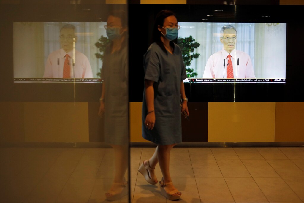A woman with a face mask walks past a screen showing a telecast of Singapore's Prime Minister Lee Hsien Loong addressing the outbreak of coronavirus disease (COVID-19), at the central business district in Singapore, April 3, 2020.