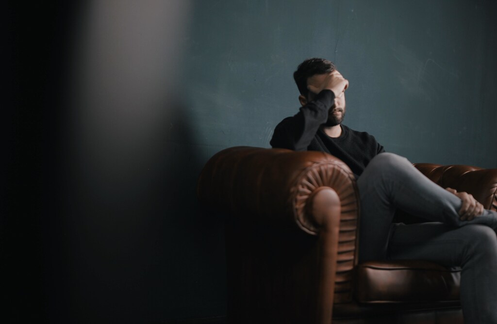 A man holds his head while sitting on a sofa
