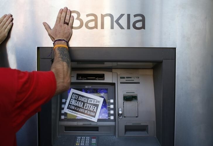 An anti-eviction activist from the Mortgage Victims Platform (PAH) hits a Bankia cash machine after learning that the eviction of Rafael Hilario Gomez Garcia (not seen), 41, who came from Peru, has been suspended, in Madrid September 13, 2013. Gomez Garcia's eviction was suspended due to his lawyer's ongoing negotiations with nationalized lender Bankia in an effort to guarantee a lower and more affordable rent for his social rent flat. The sign reads, "For your knowledge, this bank is a cheater, scams people and throws them out of their homes." REUTERS/Juan Medina (SPAIN - Tags: CRIME LAW CIVIL UNREST REAL ESTATE BUSINESS)