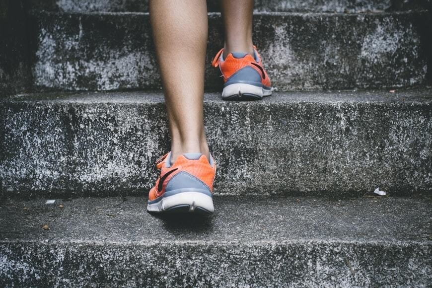 Zoomed in image of a runner, with orange trainers on grey steps.