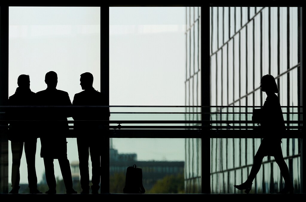 A woman walks by a group of men discussing at NATO headquarters in Brussels, Belgium, October 4, 2018. REUTERS/Francois Lenoir - RC1B5EFDF920