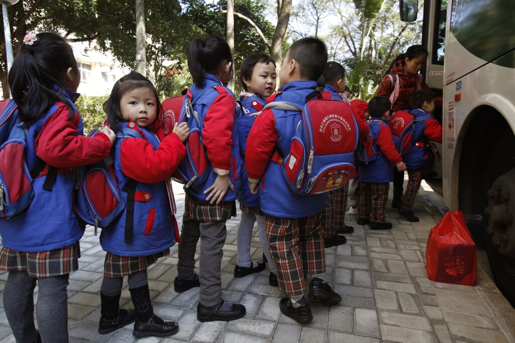 Students, who live in Shenzhen, line up for a school bus after school in Hong Kong December 19, 2013, before crossing the border back to mainland China. Every day, around 20,000 students are shuttled across the border from China, dressed in neat Hong Kong school uniforms and lugging their bags on trains and chartered buses. Roughly a quarter of births in Hong Kong between 2002 and 2012 - or more than 200,000 babies - were to families where both parents came from mainland China, who have rights to receive education in the territory. Picture taken December 19, 2013. To match story HONGKONG-EDUCATION/ REUTERS/Bobby Yip (CHINA - Tags: EDUCATION POLITICS) - RTX189VR