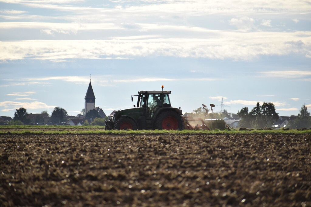 A tractor sowing a field in the cultivated landscape of southern Germany. The church tower of the city of Kuppingen is visible.