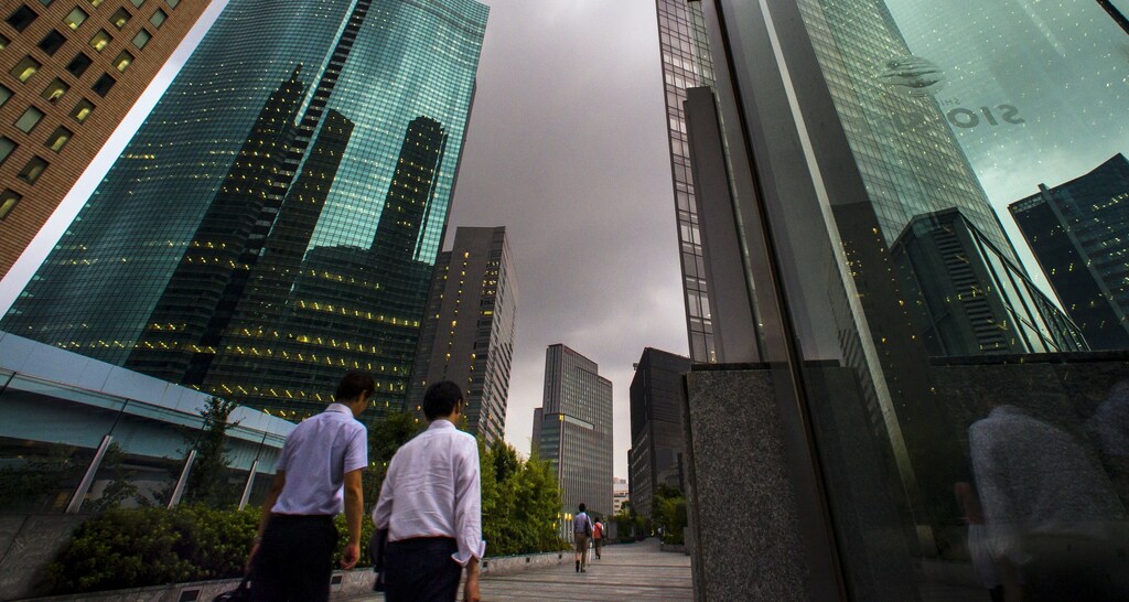 People walk in the shadows of office skyscrapers in a business district in Tokyo August 20, 2015.