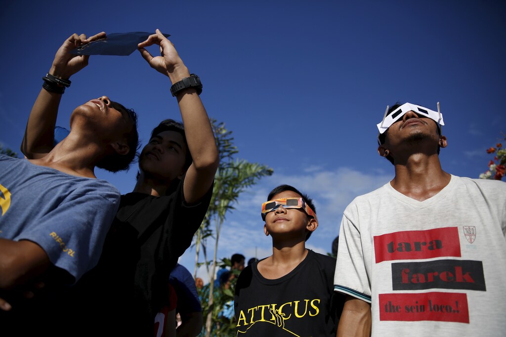 Youths watch a solar eclipse with self-made solar filters at the beach on Ternate island, Indonesia, March 9, 2016. REUTERS/Beawiharta - RTS9XHB