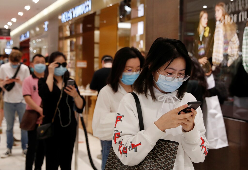 Customers, wearing protective face masks, look at their mobile phone as they line up in front of shops inside the department store Le Printemps Haussmann in Paris as France eases gradually its lockdown measures and restrictions following the outbreak of the coronavirus disease (COVID-19) in France, May 28, 2020. REUTERS/Gonzalo Fuentes - RC2MXG98PUL3
