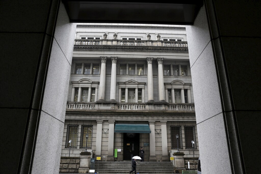 A man holding an umbrella walks in front of the Bank of Japan headquarters in Tokyo, Japan, January 29, 2016. The Bank of Japan ramped up its aggressive stimulus campaign on Friday, adding negative interest rates on central banks deposits to its massive asset-buying program, stunning financial markets that expected no action or a moderate increase in asset purchases.