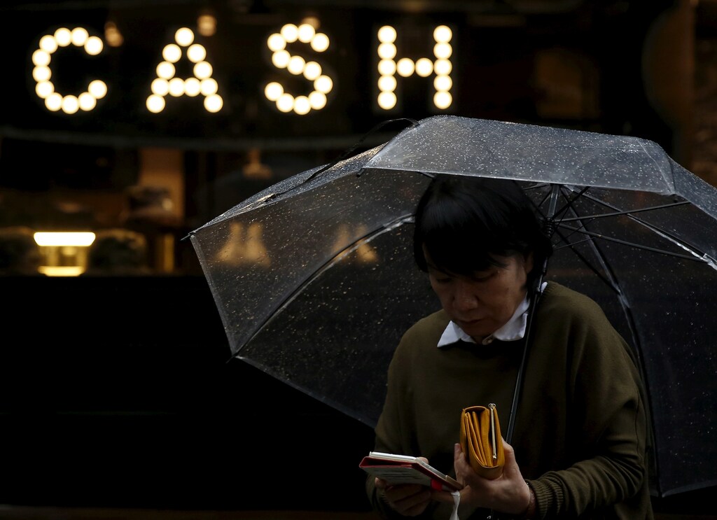 A pedestrian holding an umbrella and her wallet walks past the word "CASH", part of a sign on a street at a shopping district in Tokyo, Japan, March 7, 2016. REUTERS/Yuya Shino/File Photo GLOBAL BUSINESS WEEK AHEAD PACKAGE Ã SEARCH ÃBUSINESS WEEK AHEAD 3 OCTÃ FOR ALL IMAGES - S1BEUETMAOAA
