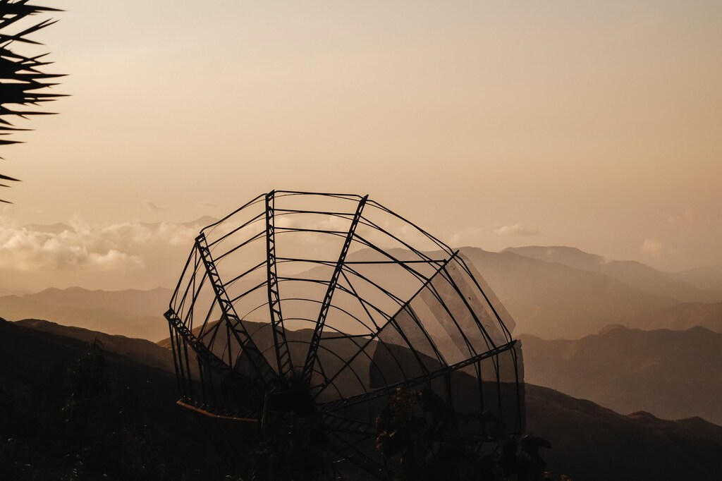 Silueta de una montaña durante la puesta de sol con una antena parabólica en primer plano.