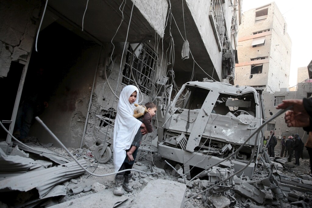A girl carrying a baby inspects damage in Damascus, Syria January 10, 2016.