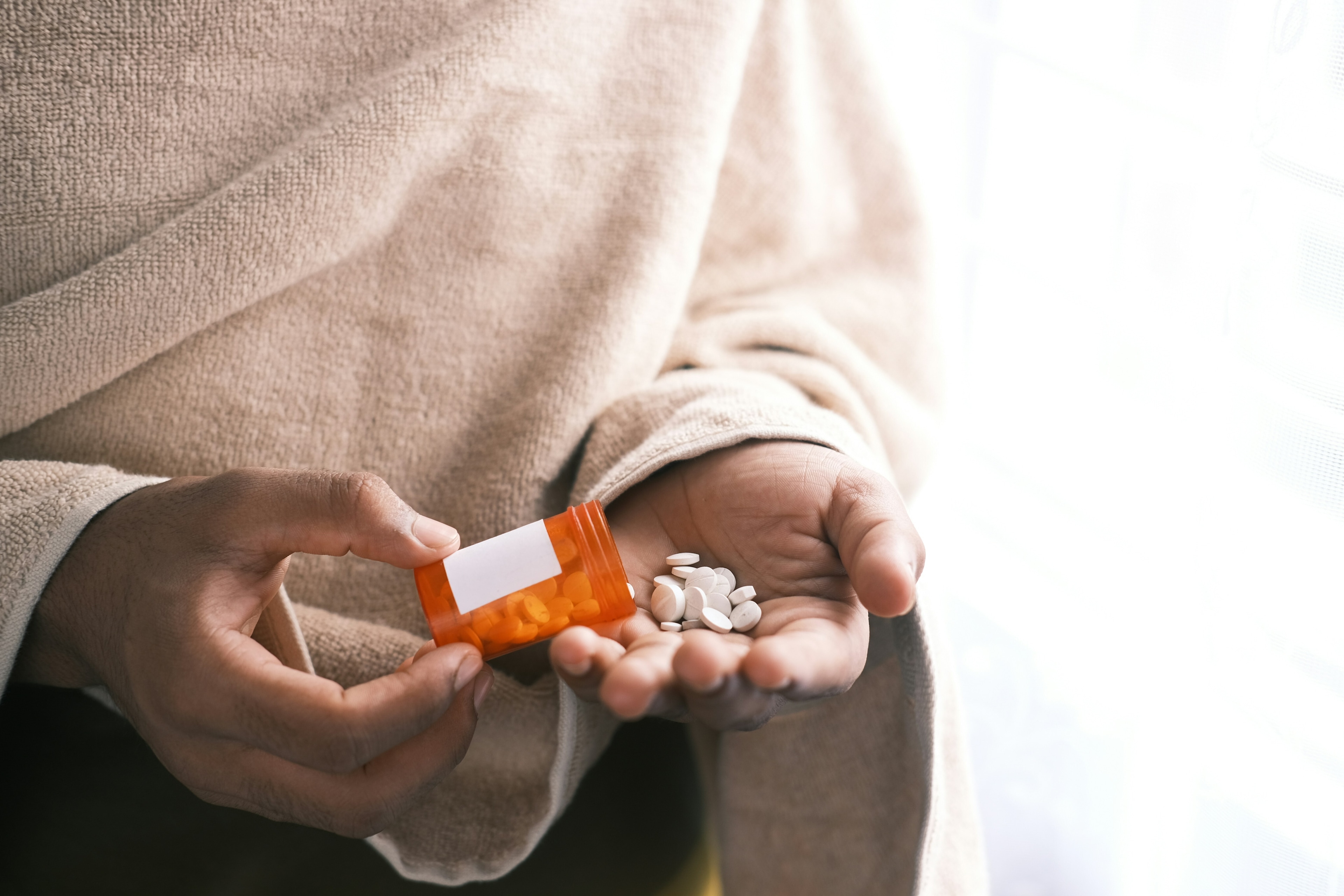 Person's hand with pills spilled out of container: The effects of antimicrobial resistance are not spread equally across society.