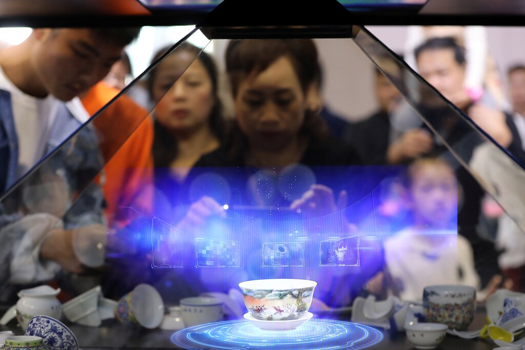 Visitors hold their phones in front of a hologram showing a porcelain teacup that is projected inside a glass cabinet during the World Conference on VR Industry in Nanchang, Jiangxi province, China October 20, 2019. Picture taken October 20, 2019. REUTERS/Stringer