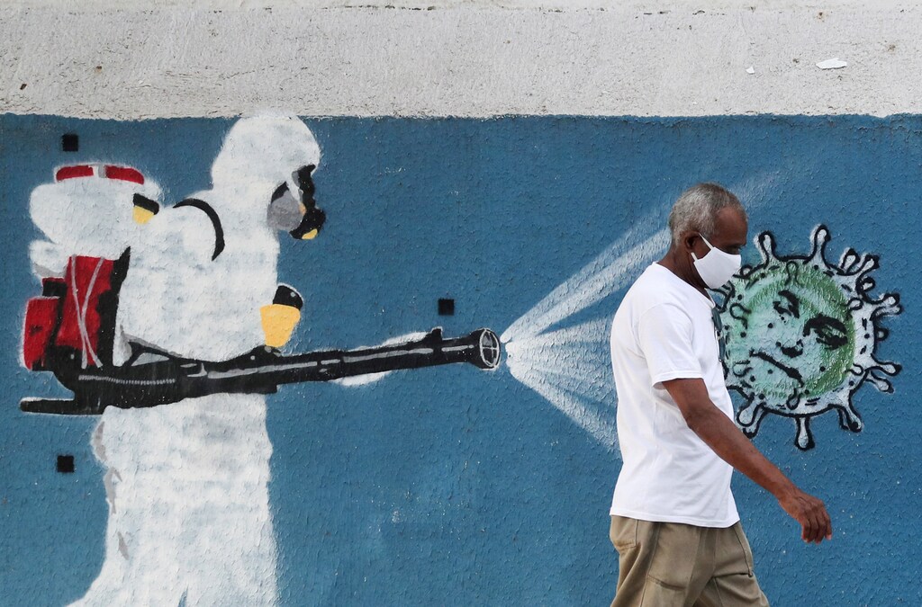 A man walks next to a graffiti depciting a cleaner wearing protective gear spraying viruses with the face of Brazil's President Jair Bolsonaro amid the coronavirus disease (COVID-19) outbreak, in Rio de Janeiro, Brazil, June 12, 2020. REUTERS/Sergio Moraes TPX IMAGES OF THE DAY - RC2S7H971KWK