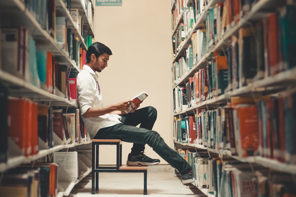 Student sitting and reading in between library bookshelves.