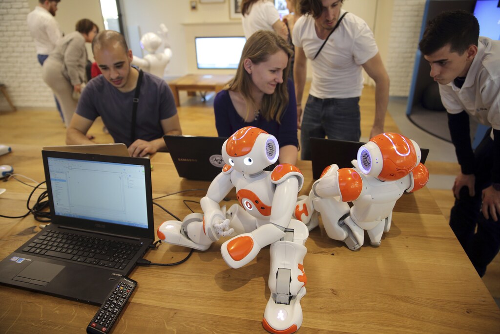Visitors and staff work on computers next to humanoid robots "Nao" in the developing space at the workshop of Aldebaran Robotics company during its opening week in Issy-Les-Moulineaux near Paris July 2, 2014. The Aldebaran Workshop opens three main spaces, discovering, learning and developing, for the public to interact with humanoid robots and to introduce a new generation of emotionally-savvy robots which organisers hope one day could become man's new best friend. Picture taken July 2, 2014. REUTERS/Philippe Wojazer (FRANCE - Tags: BUSINESS INDUSTRIAL) - PM1EA721A2J01