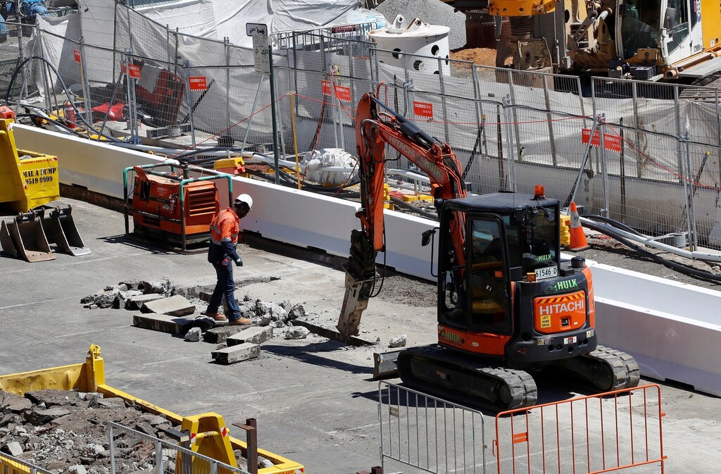 A worker looks on as a drill breaks the pavement on a construction site next to Barangaroo building complex in Sydney, Australia