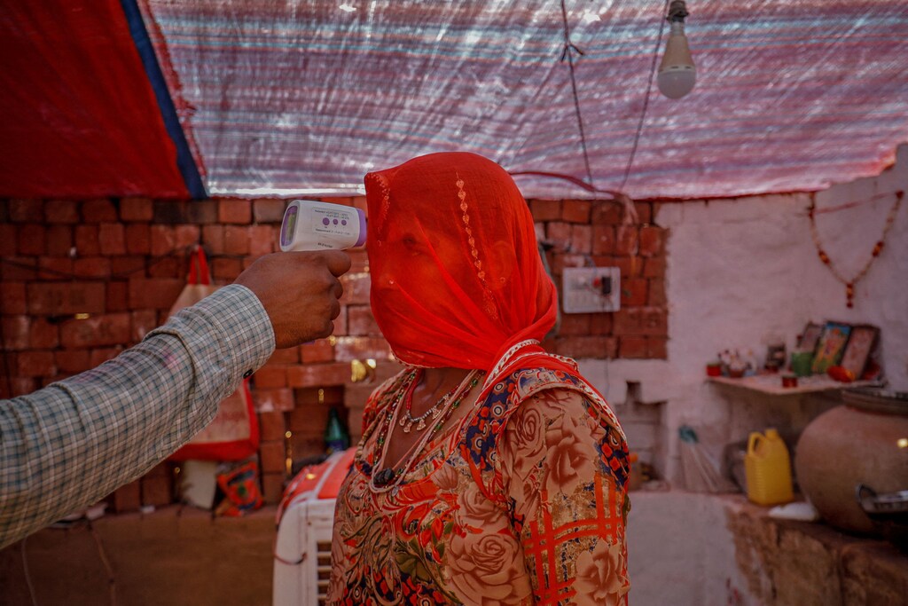 A healthcare worker checks the temperature of a woman inside her hut during a coronavirus disease vaccination drive for workers at a brick kiln in Kavitha village on the outskirts of Ahmedabad, India, April 8, 2021. Women's health and wellbeing was set back globally during the pandemic.