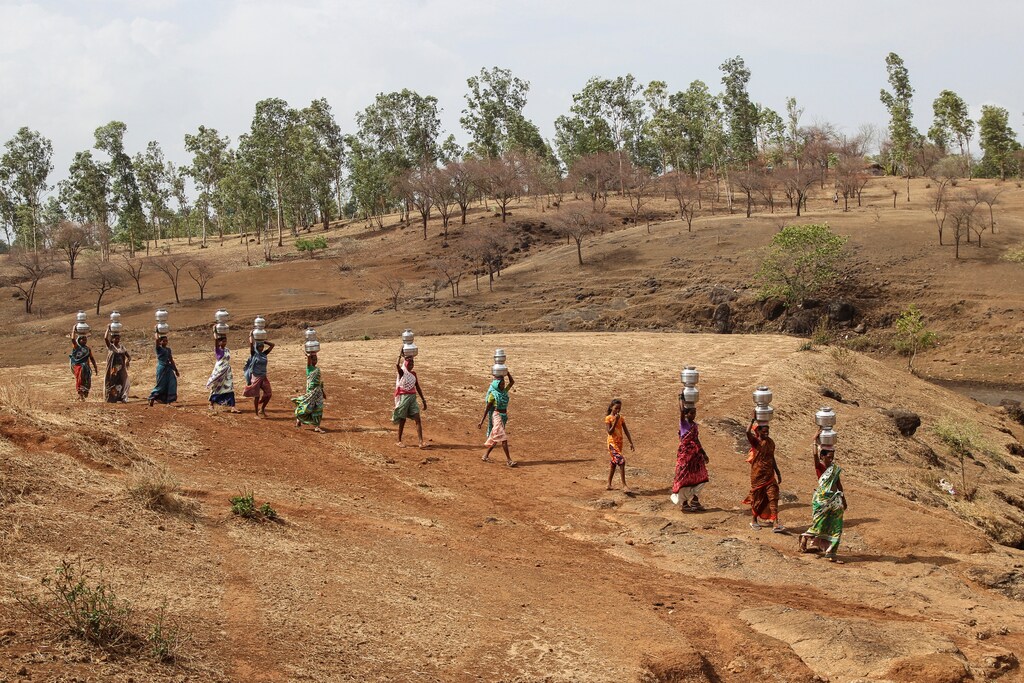 Women carry pitchers filled with water from an opening made to filter water next to a polluted lake in Thane, India June 13, 2019. REUTERS/Prashant Waydande - RC1CB58CD440