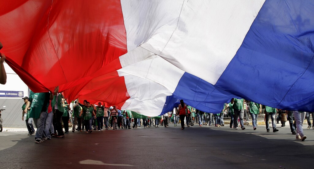 People hold a large Paraguayan flag during a demonstration against a new tax law, in downtown Asuncion, Paraguay, October 19, 2015. The protesters, who are owners and employees from about 300 cooperative businesses, said that they are demonstrating against a new law that establishes a value-added tax of 10 per cent to their services. REUTERS/Jorge Adorno - RTS54V9