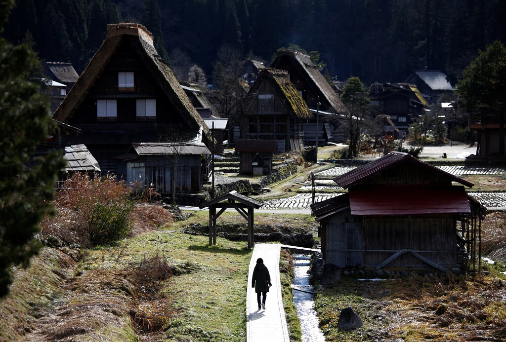 A visitor strolls near traditional Gassho style houses in Shirakawa-go (Shirakwa Village), one of Japan's UNESCO World Heritage sites, Gifu Prefecture, Japan December 2, 2017. Picture taken December 2, 2017. REUTERS/Issei Kato - RC1B7D4E7330