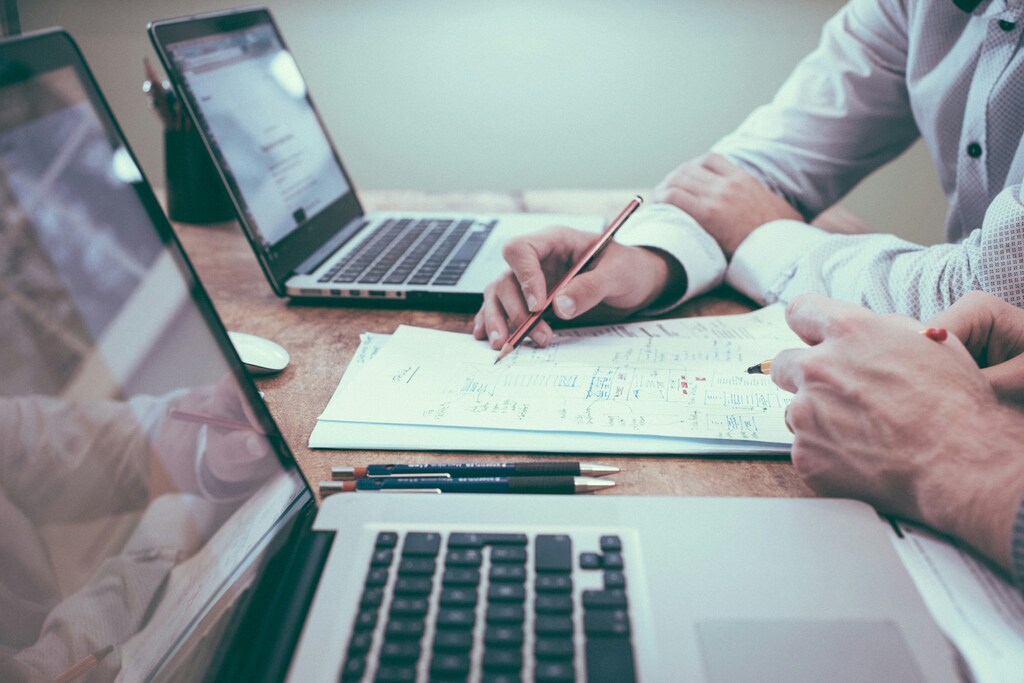 Dos personas sentadas en una mesa con laptops, papel, bolígrafos y lápiz. Los líderes empresariales necesitan desarrollar mejores estrategias para medir el impacto en el sector de la inversión de impacto.