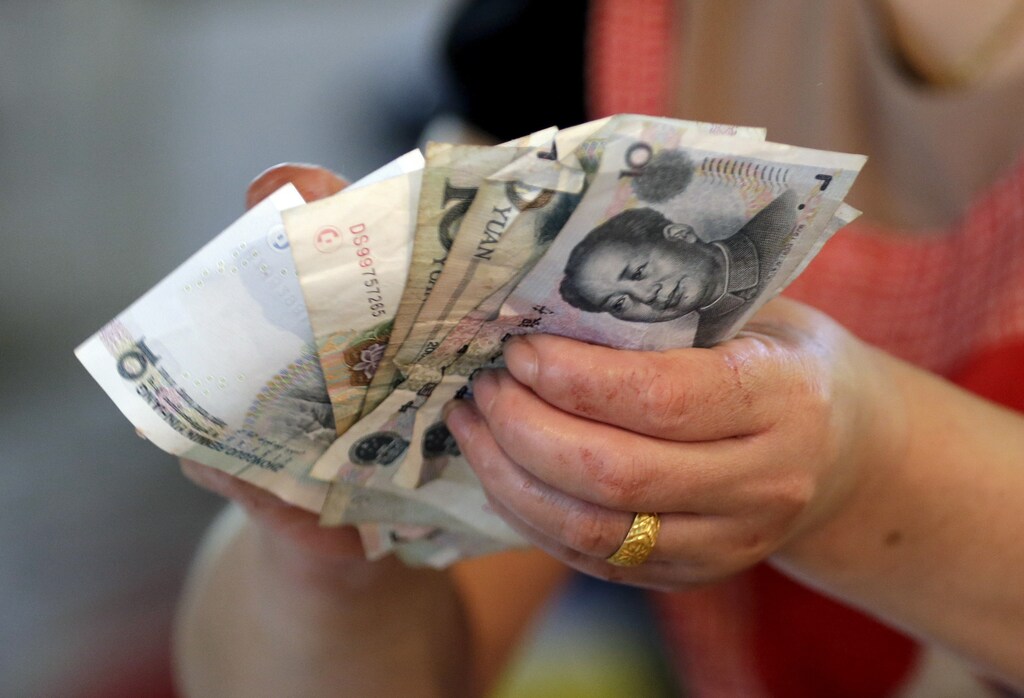 A vendor holds Chinese Yuan notes at a market in Beijing, August 12, 2015. China shocked global markets on Tuesday by devaluing its currency after a run of poor economic data, a move it billed as a free-market reform but which some experts suspect could be the beginning of a longer-term slide in the exchange rate. REUTERS/Jason Lee - GF20000020395