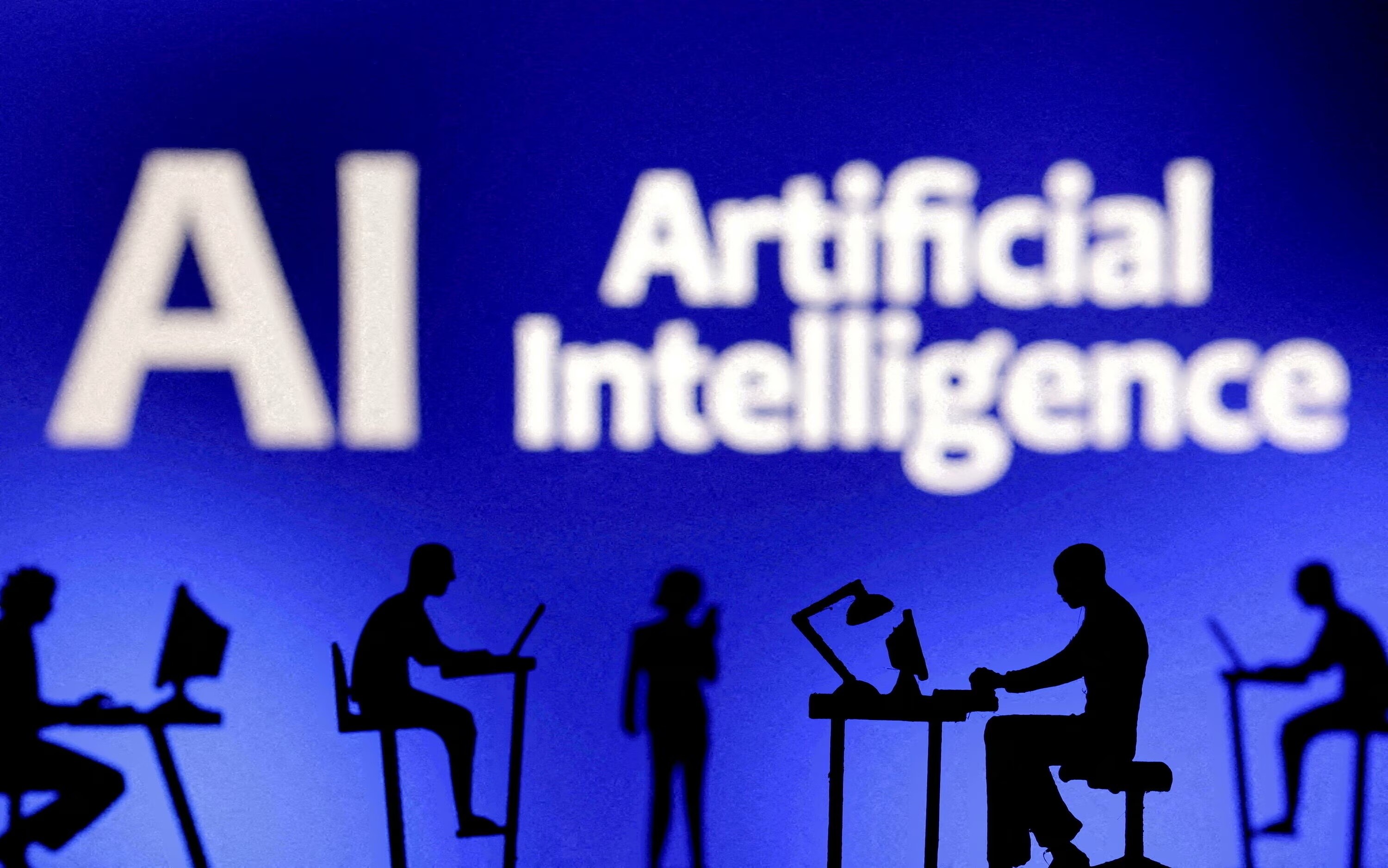 Figuras con computadoras y teléfonos inteligentes se ven frente a las palabras "Inteligencia Artificial IA" en esta ilustración tomada el 19 de febrero de 2024: se espera que la IA agéntica contribuya a la competitividad nacional.