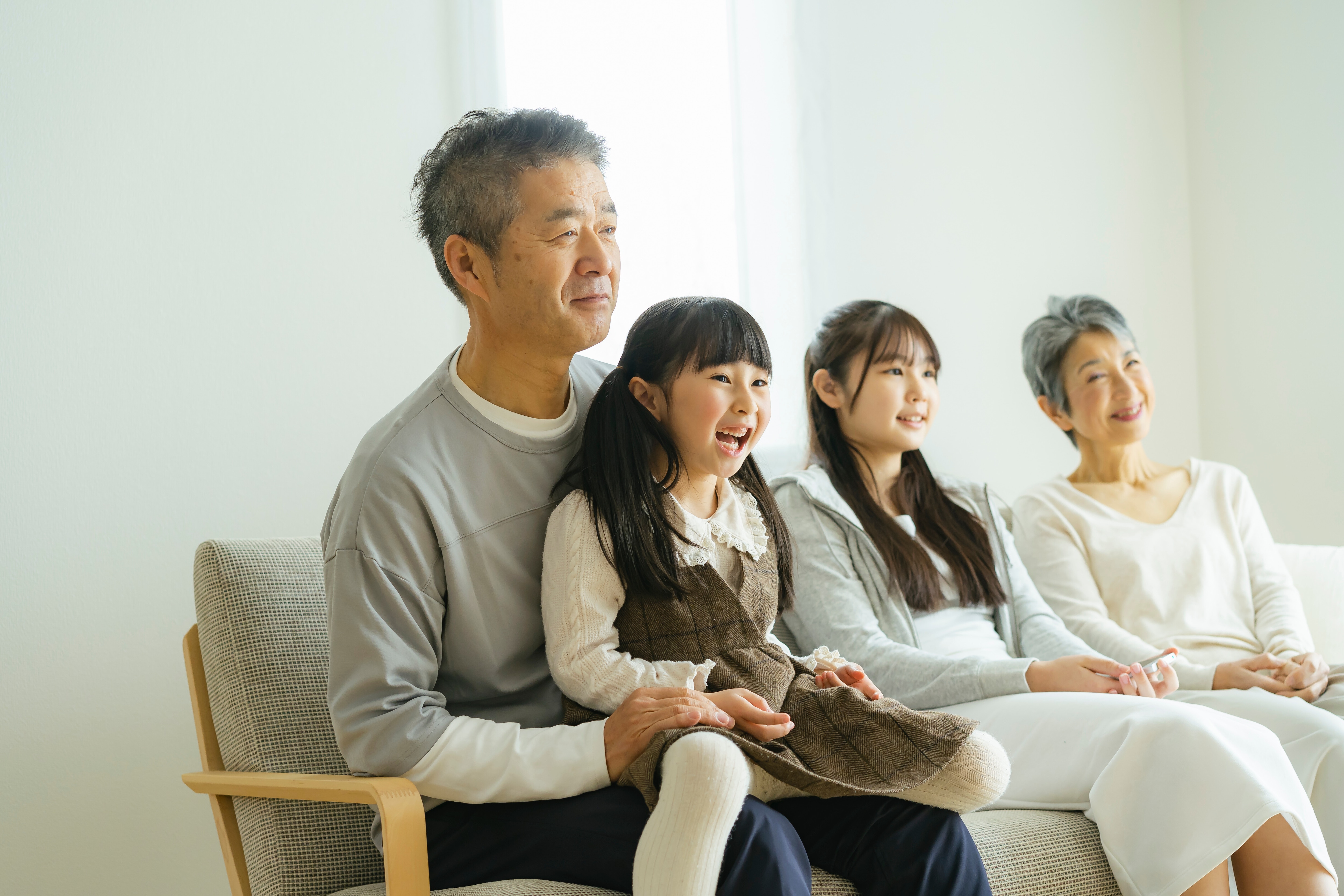 A family of four - two grandparents and two grandchildren - sit on a sofa together smiling.