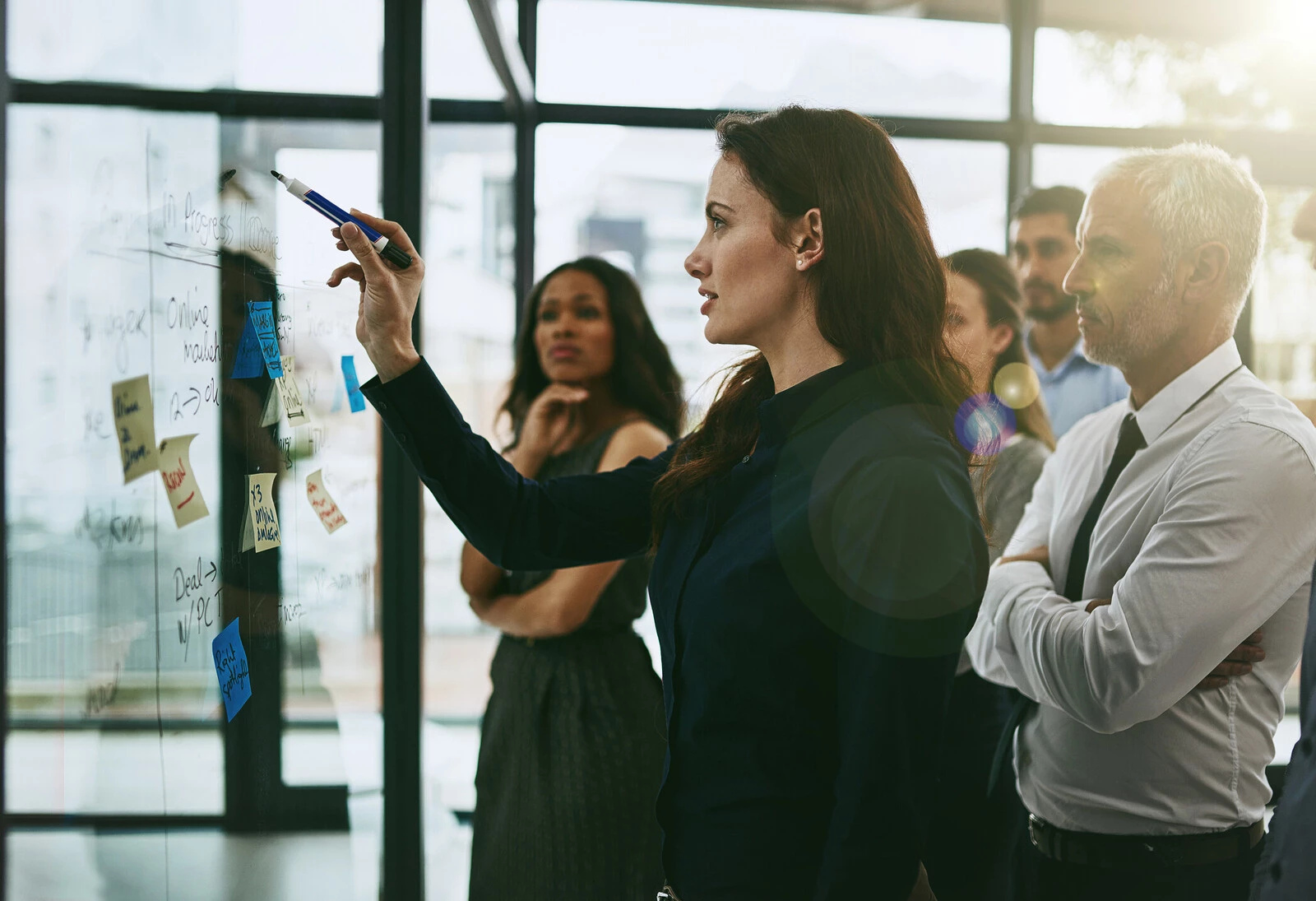 A woman points at a whiteboard while her colleagues look on.