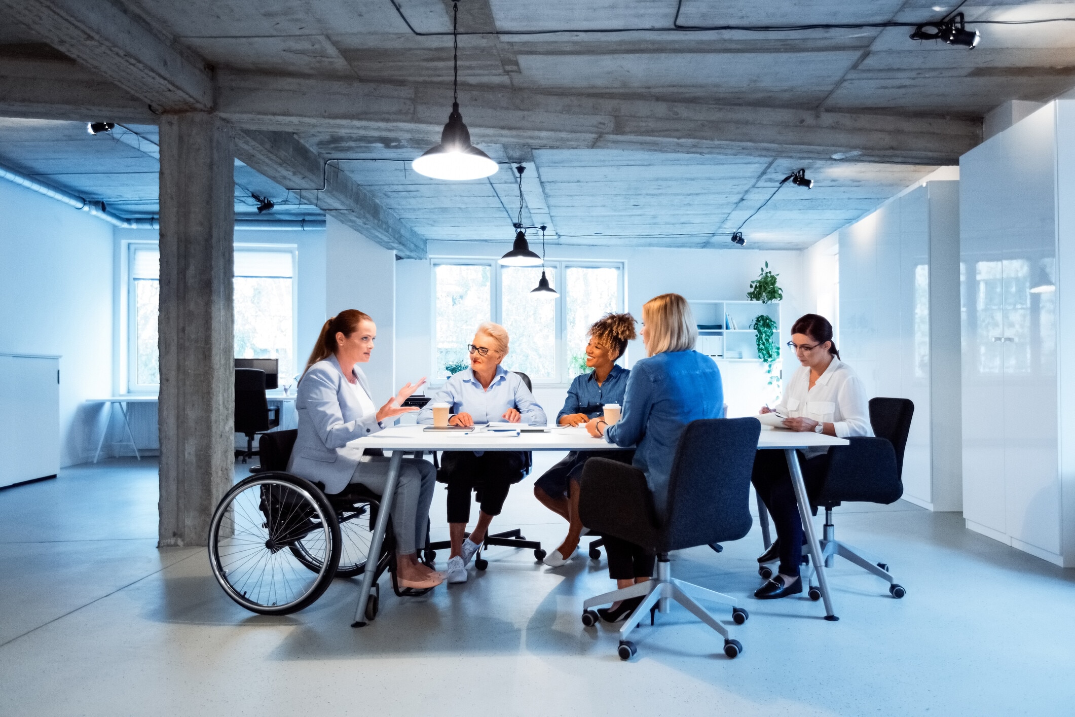 Business owner in wheelchair talking with colleagues at desk. Business professionals are having meeting in office: AI for business needs skilled people, which means investment